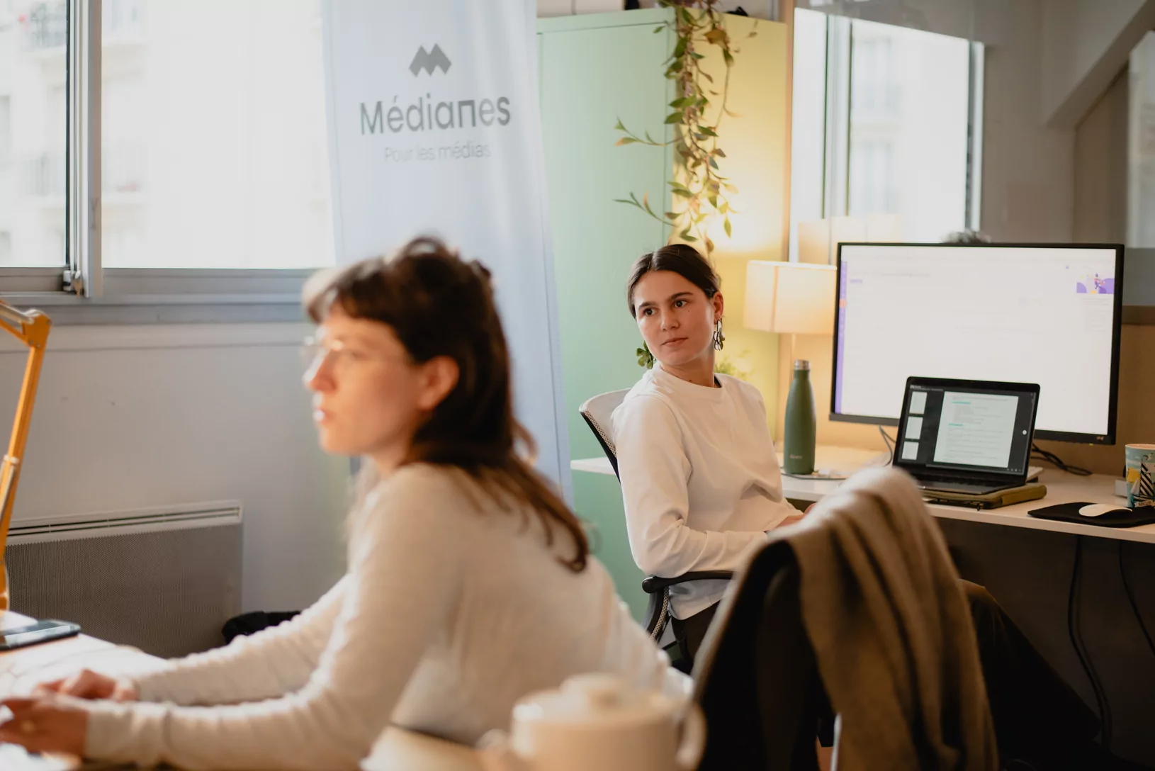 Deux personnes au travail devant le kakemono « Médianes, pour les médias ».