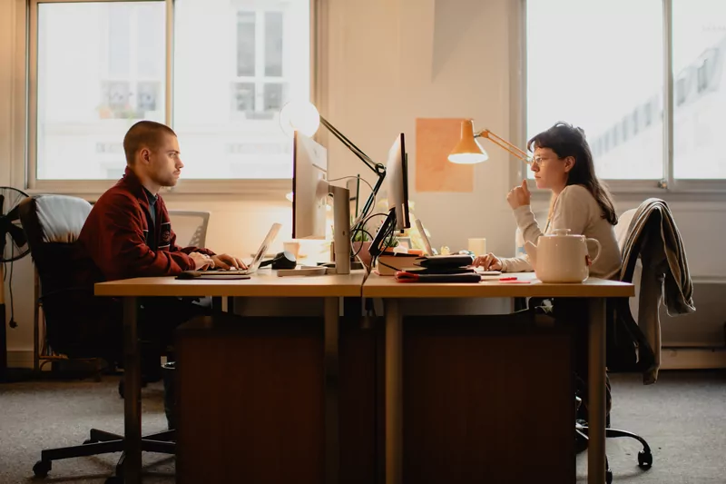Deux personnes travaillent face à face à leurs postes, fenêtres en enfilade.