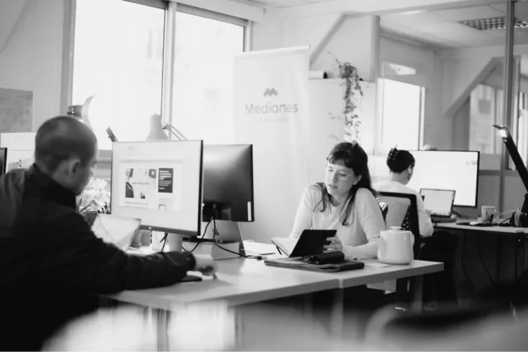 L’open space de Médianes : trois personnes au travail devant leurs écrans, kakemono Médianes en fond.